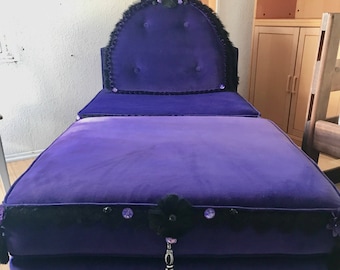 May include: A purple velvet chaise lounge with a tufted backrest and matching ottoman. The chaise features black lace trim, decorative embellishments, and a tassel. The furniture is a deep shade of purple.