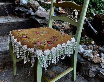 Könnte beinhalten: Ein grüner Holzstuhl mit einem floralen Kissen und einer weißen Spitzenborte. Der Stuhl steht auf einer Steintreppe.