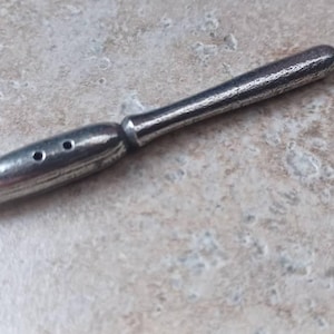 May include: A silver metal pen nib with a pointed tip and two holes on the side. The nib is attached to a long, silver metal handle.