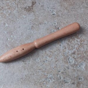 May include: A wooden knitting needle with a pointed tip and a smooth handle. The needle has two holes near the tip.