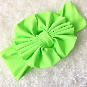 May include: A bright green fabric headband with a large, knotted bow. The headband is made of a soft, stretchy material and is perfect for adding a pop of colour to any outfit.