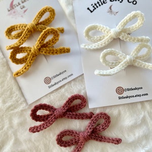 May include: Three pairs of handmade crochet bow hair clips in mustard yellow, cream, and mauve. Each pair is attached to a white card with the text "Little Sky Co" and an Instagram handle.