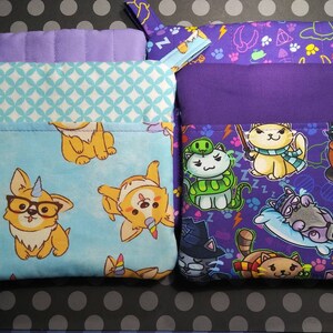May include: Two purple and blue pot holders with different patterns. One pot holder has a light blue background with a pattern of cartoon dogs wearing glasses and unicorn horns. The other pot holder has a purple background with a pattern of cartoon cats with different accessories and a Harry Potter theme.