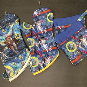 May include: A set of three kitchen textiles: two oven mitts and a pot holder. The items feature a blue and yellow Starry Night-inspired design with Star Wars characters. The oven mitts have a white trim, and the pot holder has a blue top.