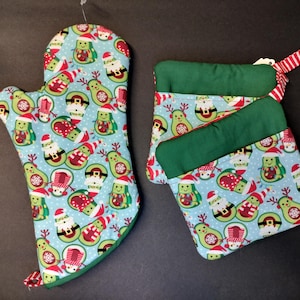 Può includere: Set di tre guanti da forno verdi e blu con un motivo di avocado natalizio. I guanti presentano uno sfondo blu chiaro con fiocchi di neve bianchi e avocado verdi che indossano cappelli di Babbo Natale e corna di renna.