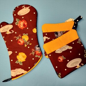 May include: A set of two brown and yellow oven mitts with a floral and spaceship pattern. The mitts are made of fabric and have a quilted texture.