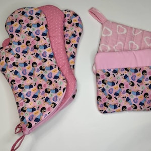 May include: Pink oven mitt and pot holders. The oven mitt features a cartoon character pattern on a pink background. The pot holders have a pink heart pattern and a matching cartoon character pattern. All items have pink trim.