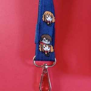 Könnte beinhalten: Ein blaues Lanyard mit einem silbernen Clip. Das Lanyard hat ein sich wiederholendes Muster von Comicfiguren aus der Harry-Potter-Serie.
