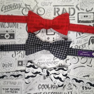 Pode incluir: Três gravatas borboleta em um fundo branco com rabiscos em preto e branco. As gravatas borboleta são vermelhas com código binário branco, xadrez preto e branco e brancas com bigodes pretos. O texto "He's my superhero" está escrito no fundo.