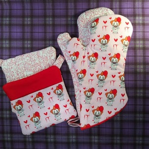 Könnte beinhalten: Zwei rosa Topflappen mit rotem Rand und einem Muster aus einem Clown mit dem Wort "IT" und roten Herzen. Ein Topflappen ist ein Topfuntersetzer mit roter Auskleidung.