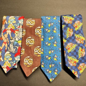 Op de afbeelding: Vier zijden stropdassen met verschillende cartoonfigurenontwerpen. De stropdassen zijn blauw, bruin en rood met witte accenten.