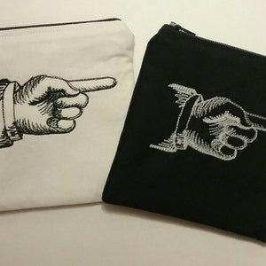 May include: Two zippered pouches, one white and one black, with an embroidered pointing hand design. The hand is pointing to the right.