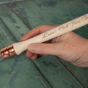 May include: A wooden paint brush with a copper ferrule and natural bristles. The brush handle is engraved with the text "Laura's Chalk Paint Brush".