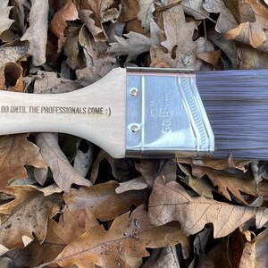 A paint brush with a wooden handle, featuring engraved text.
