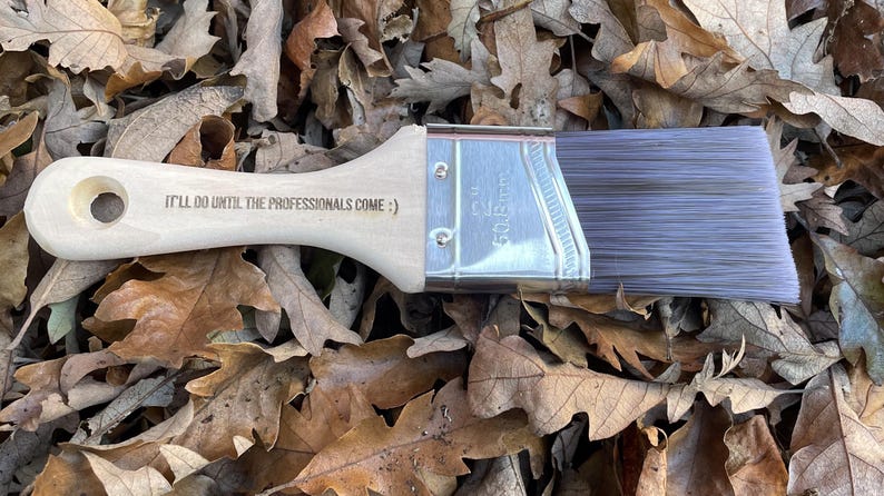 A paint brush with a wooden handle, featuring engraved text.