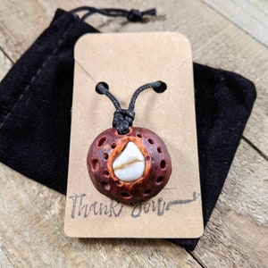 May include: A brown and white pendant with a black cord, displayed on a brown card with the text "Thank You". The pendant is made of wood and has a white stone in the center.