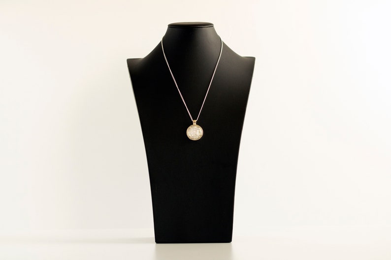 May include: A silver chain necklace with a round, gold pendant on a black mannequin bust. The pendant is covered in small, white stones.