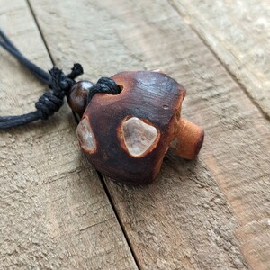 May include: A brown ceramic mushroom pendant with clear crystal accents hangs from a black cord necklace.