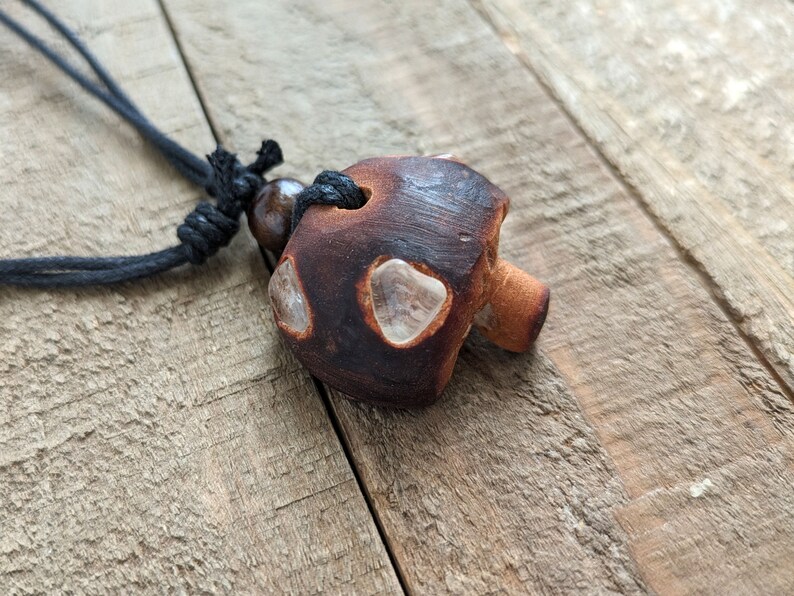 May include: A brown ceramic mushroom pendant with clear crystal accents hangs from a black cord necklace.