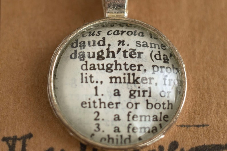 Puede incluir: Un colgante de plata con un c&iacute;rculo de vidrio que contiene una definici&oacute;n del diccionario de la palabra "hija". La definici&oacute;n dice: "hija (dɔːtə) hija, probablemente lit., orde&ntilde;adora, de 1. una ni&ntilde;a o una u otra o ambas 2. una mujer 3. una ni&ntilde;a"