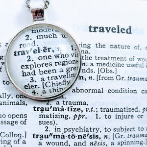 May include: A silver necklace with a round pendant featuring the word "traveler" defined in a vintage dictionary. The definition includes the words "one who explores regions" and "a traveling elder".