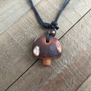May include: A brown and white ceramic mushroom pendant necklace with a black cord.