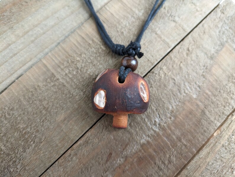 May include: A brown and white ceramic mushroom pendant necklace with a black cord.
