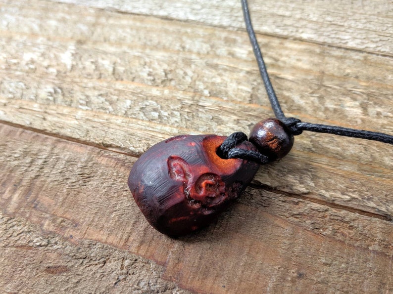 May include: A dark red wooden pendant with intricate carvings hangs from a black cord with a brown wooden bead.