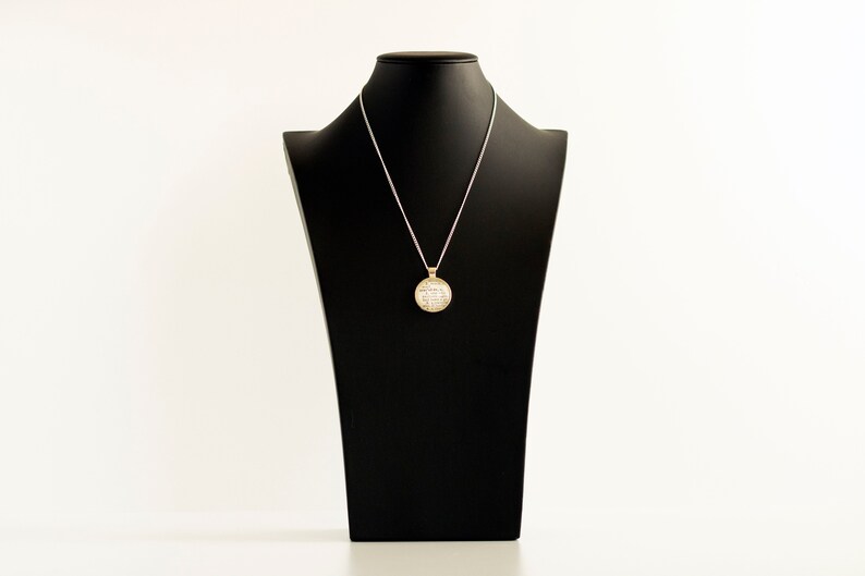 May include: A silver chain necklace with a round, gold pendant featuring a white, sparkly design. The necklace is displayed on a black mannequin bust.