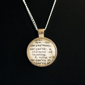 May include: A silver necklace with a round pendant featuring a dictionary definition of the word "sarcastic". The pendant is made of glass and has a vintage look.
