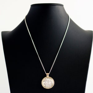 May include: A silver chain necklace with a round pendant featuring a definition of the word "explorer".