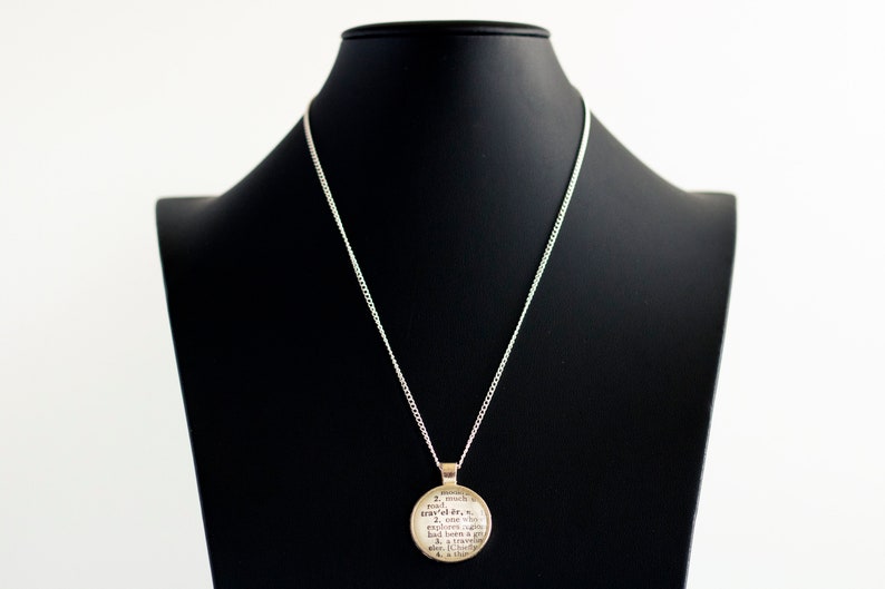 May include: A silver chain necklace with a round pendant featuring a definition of the word "explorer".