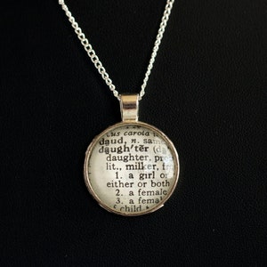Puede incluir: Un collar de cadena de plata con un colgante redondo que presenta una definici&oacute;n del diccionario de la palabra "hija".