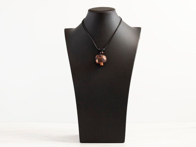 May include: A brown wooden mushroom pendant necklace on a black cord. The pendant is on a black mannequin bust.