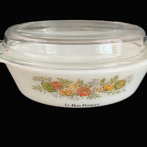 May include: White oval casserole dish with a glass lid. The dish has a floral design with vegetables and the words "Le Bon Potager" printed on the bottom.