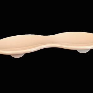 May include: A light peach-colored, elongated serving tray with a curved design. The tray has a smooth, glossy finish and is supported by two small, rounded feet. The overall shape is reminiscent of a spoon or a stylized leaf.