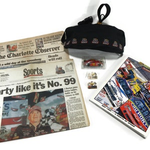 May include: A collection of NASCAR memorabilia including a newspaper headline "Party like it's No. 99", a small toy car, a black zippered pouch with the NASCAR logo, and a magazine with the text "May 1999 - A Month of Speed".