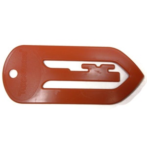 May include: An orange plastic bookmark with the word "Tupperware" printed on it. The bookmark has a cut-out design that resembles a key.