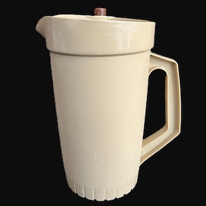 May include: A beige plastic pitcher with a handle and a lid. The pitcher has a spout for pouring and a textured surface. The lid is brown. The pitcher is designed for holding liquids.