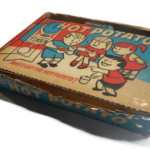 May include: A vintage Remco Hot Potato game box. The box has a colourful illustration of children playing the game, with the words "Hot Potato" and "Who's Got The Hot Potato?" printed on it. The box is made of cardboard and has a retro design.