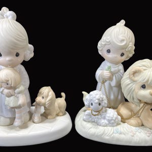 Puede incluir: Dos figuritas de porcelana de personajes de Precious Moments. La primera figurita es una ni&ntilde;a que sostiene una mu&ntilde;eca. La segunda figurita es un ni&ntilde;o que sostiene un cordero. Ambas figuritas est&aacute;n sobre bases blancas.