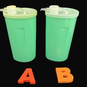 May include: Two mint green plastic tumblers with matching lids and flip-top spouts. The tumbler on the left has a pale yellow lid, while the one on the right has a white lid. An orange letter A is placed below the left tumbler and a B below the right.