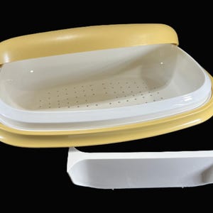 May include: A yellow and white plastic food storage container with a lid and a separate white tray. The container has a rectangular shape with rounded corners. The lid is open, revealing the interior.
