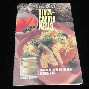 May include: A Tupperware cookbook titled "Stack-Cooked Meals" features a photo of a meal with pasta, broccoli, and chicken. The cover also shows a bowl of watermelon and a stackable microwave cooker. The text reads "Thousands of exciting mix-and-match microwave menus."