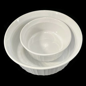 May include: Two white ceramic baking dishes, one nested inside the other. The larger dish has a fluted rim.