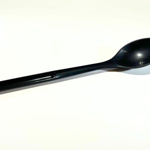 May include: A black plastic spoon with a long handle and a rounded bowl. The spoon has a hole at the end of the handle for hanging. The spoon is approximately 12 inches long.
