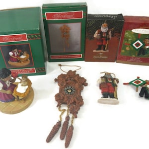 May include: A collection of six Christmas ornaments, including a cuckoo clock, a poinsettia girl and manger, a Swiss Santa, a boy with a kite, and a Santa with a sack. The ornaments are packaged in boxes with the words "Christmas" and "Ornament" on them.