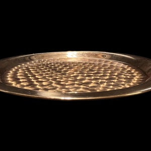 May include: A round, hammered brass serving tray with a raised rim. The tray has a warm, golden color and a textured surface.