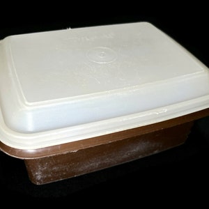 May include: A brown plastic rectangular food storage container with a white lid. The lid has a slight curve to it.