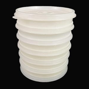 May include: A stack of eight circular, semi-translucent white plastic lids. Each lid features a slightly raised center and a flat, wide rim designed for sealing containers. The lids are stacked vertically, creating a uniform cylindrical shape.
